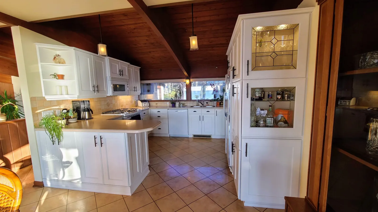 White kitchen with glass-front cabinets under a wood ceiling
